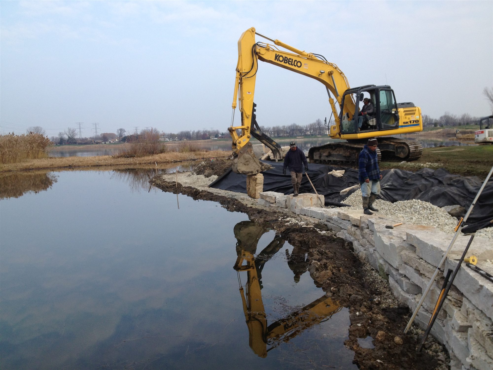 Crew and excavator installing stone beside a body of water